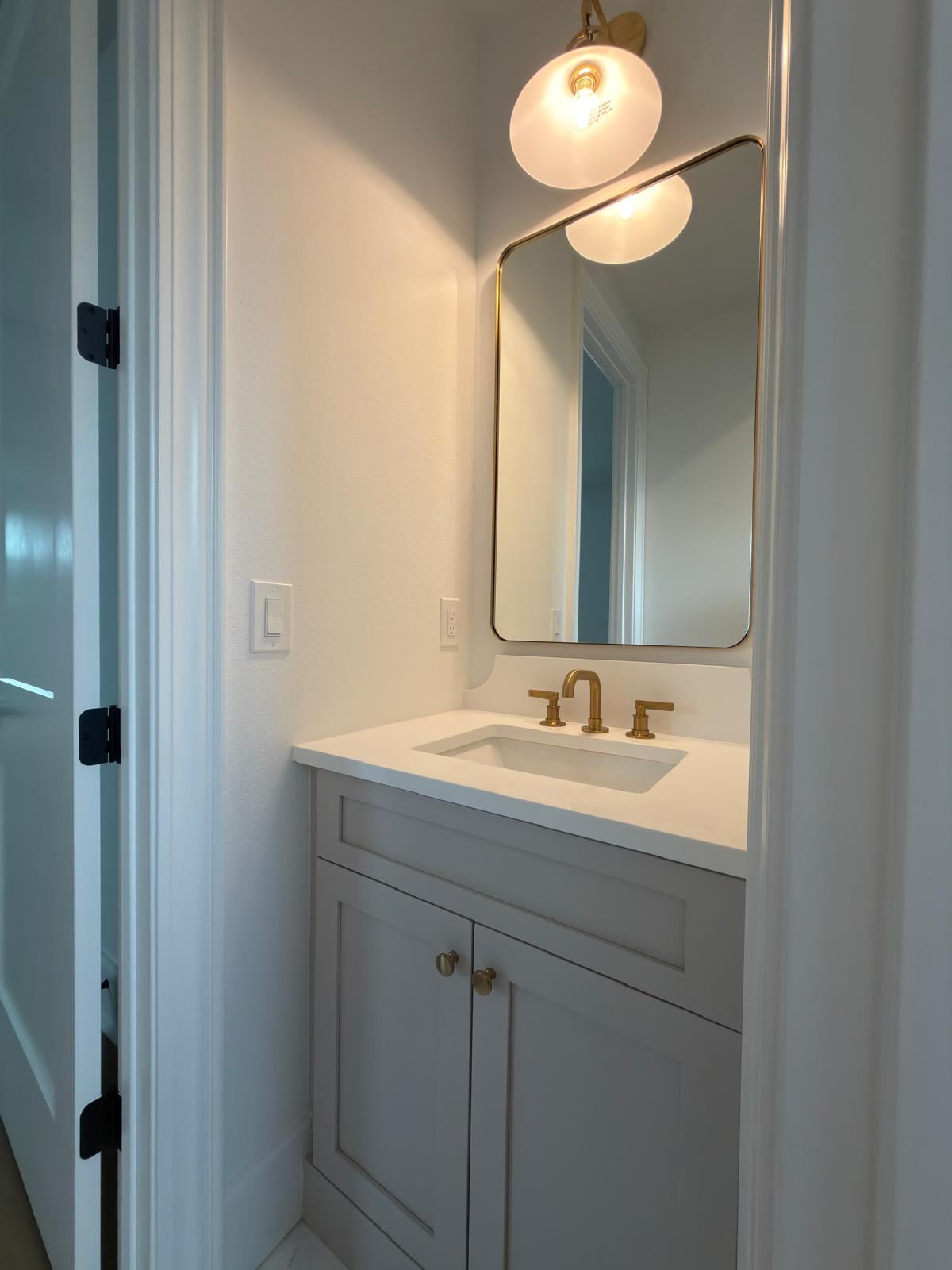 White powder room with brass mirror and sconce